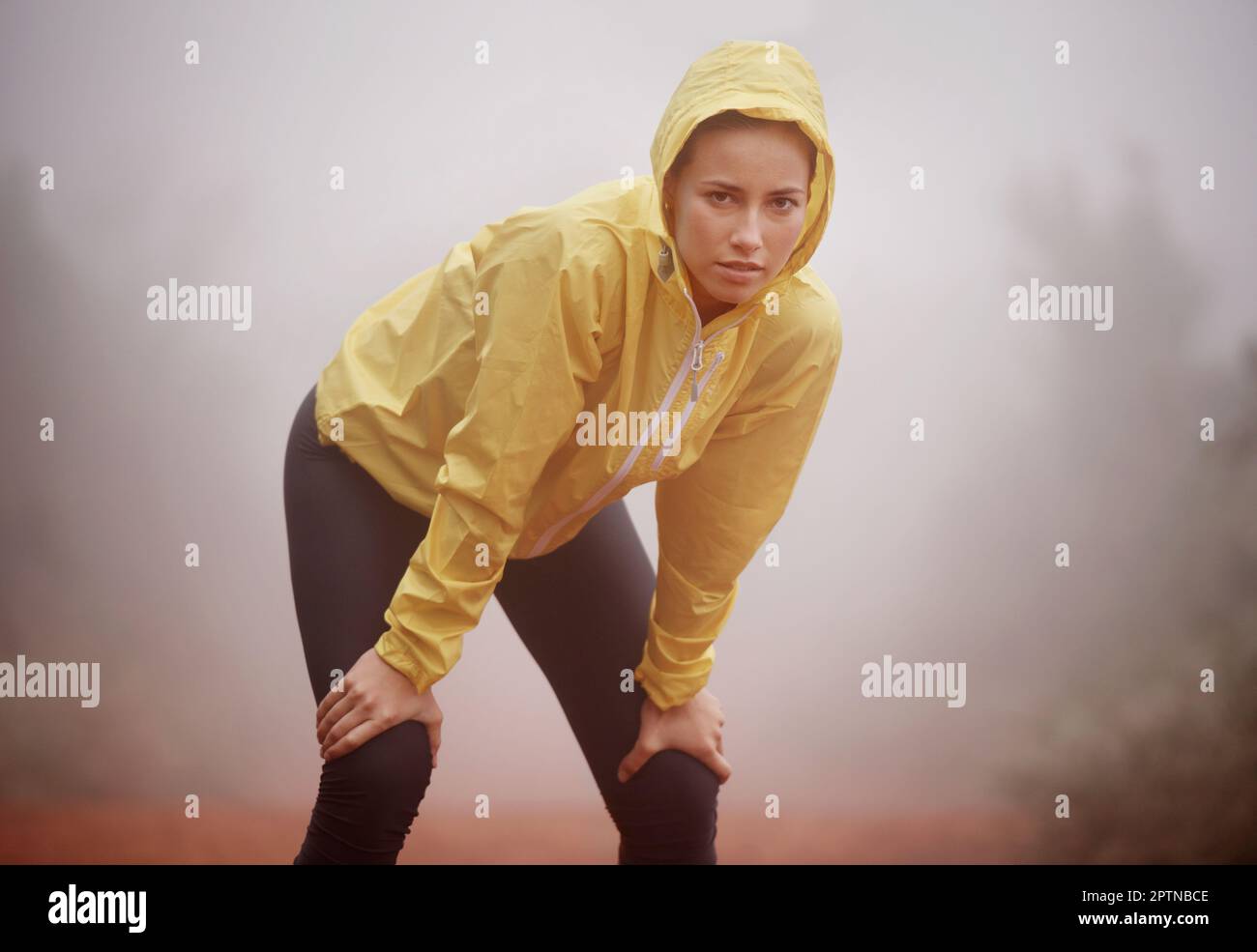 Si allena in qualsiasi tempo. Una giovane runner femminile che si ferma per un riposo mentre fuori in una corsa attraverso una foresta nebbiosa Foto Stock