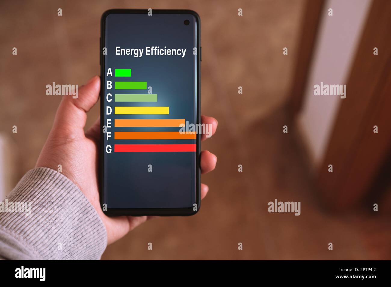 La mano della donna tiene uno smartphone con etichette di valutazione dell'efficienza energetica sullo schermo. Prodotti a basso consumo ed efficienti. Ridurre l'impronta di carbonio. Foto Stock