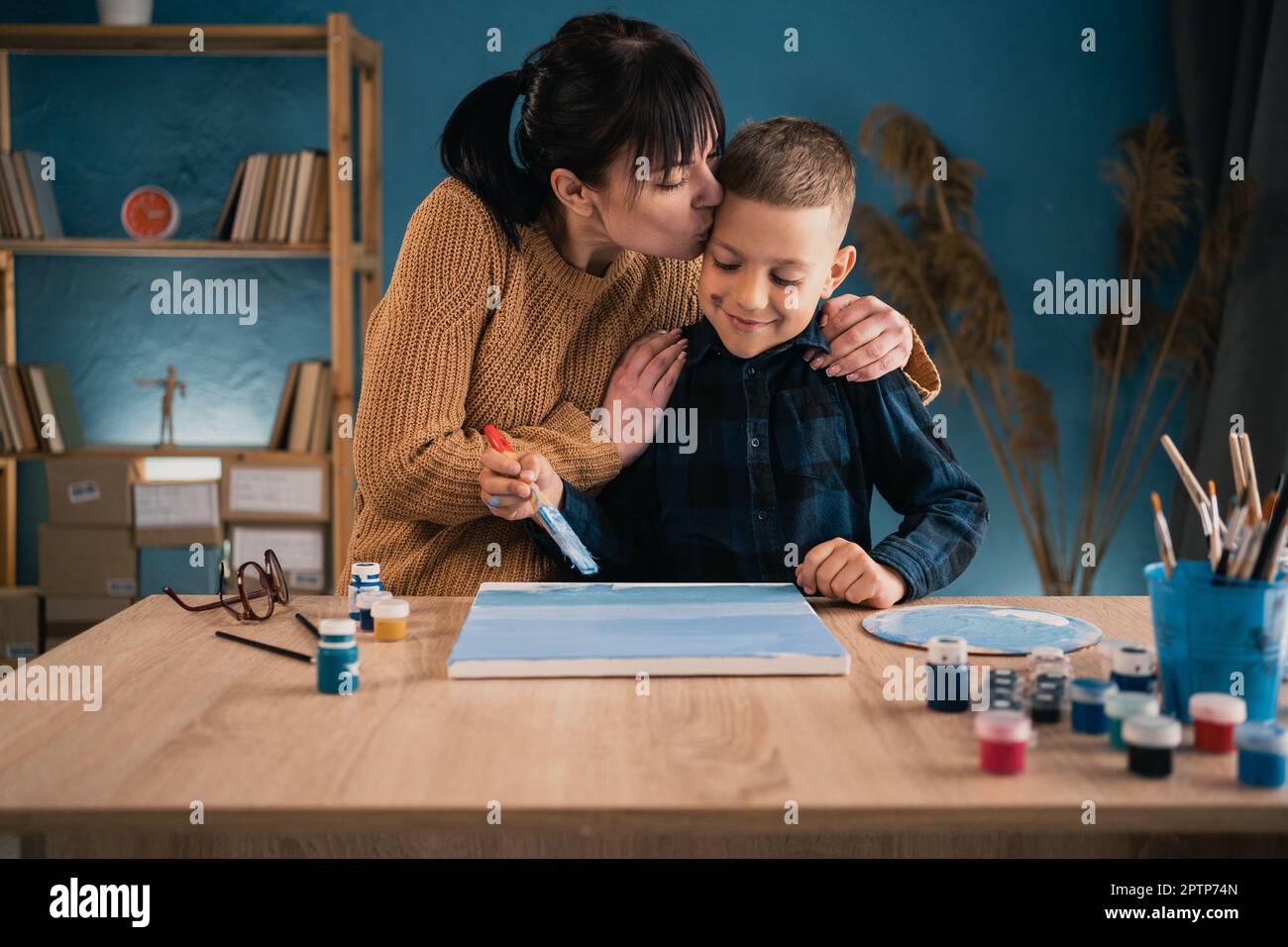 La mamma aiuta suo figlio uno scolaro a dipingere un'immagine con pitture su tela. donna che abbraccia un bambino. Hobby condivisi e ricreazione. Foto Stock