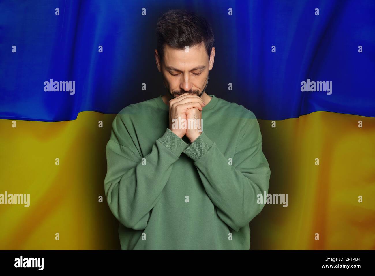 Uomo che prega contro la bandiera nazionale. Fermare la guerra in Ucraina Foto Stock