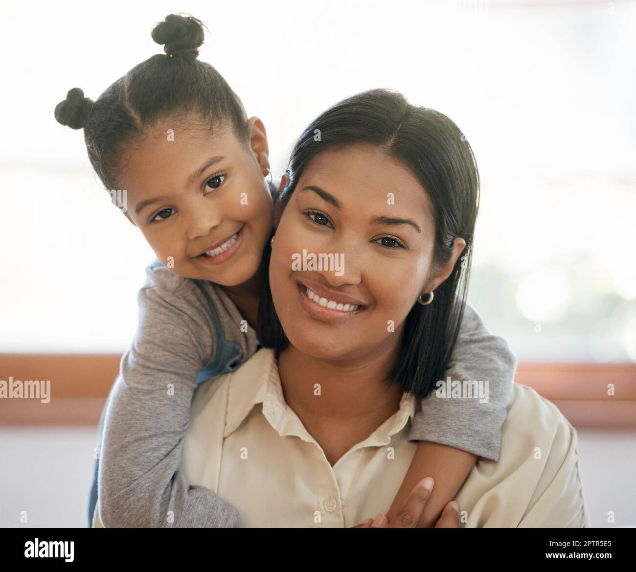 Ritratto di due giovani femmine di razza mista solo sorridendo e guardando rilassato a casa. mamma nera africana americana con la sua carina figlia ispanica h Foto Stock
