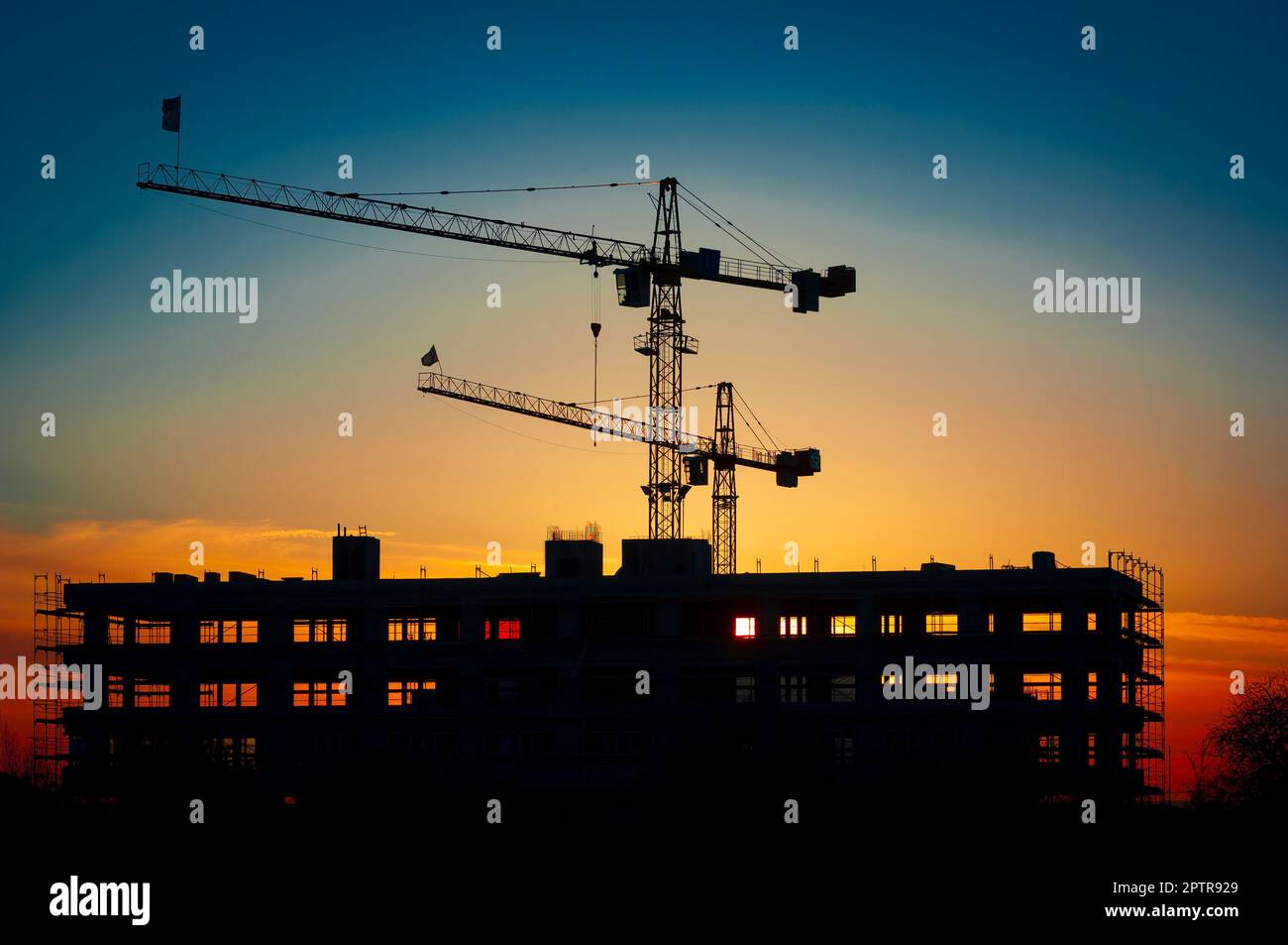 Il guscio di un edificio di uffici in controluce del sole tramontato con una gru da cantiere Foto Stock