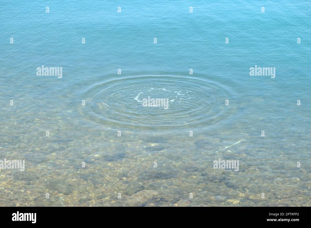 Goccioline rotonde di acqua sopra i cerchi sull'acqua. Goccia d'acqua, vortice e spruzzi. Increspature sullo sfondo con motivo a trama marina. Foto Stock