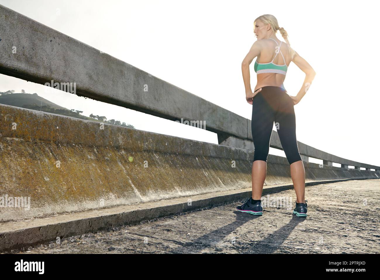 Alzarsi sopra di tutto. Vista posteriore ripresa di una giovane donna attraente in piedi su un ponte pronto per correre. Foto Stock