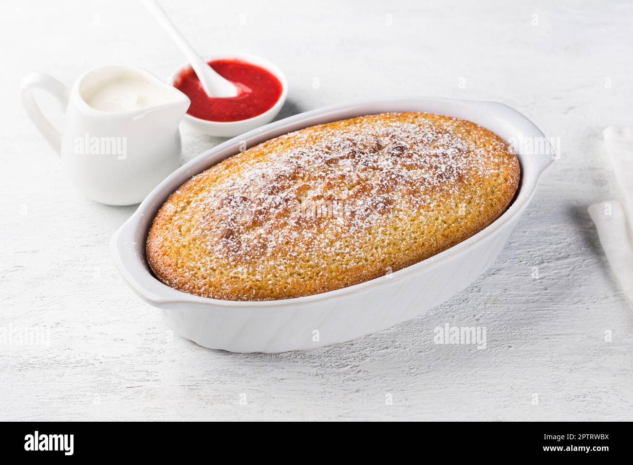 Mannik appena preparato, torta di semola in forma cosparsa di zucchero a velo con panna acida e salsa di frutti di bosco su fondo grigio chiaro Foto Stock