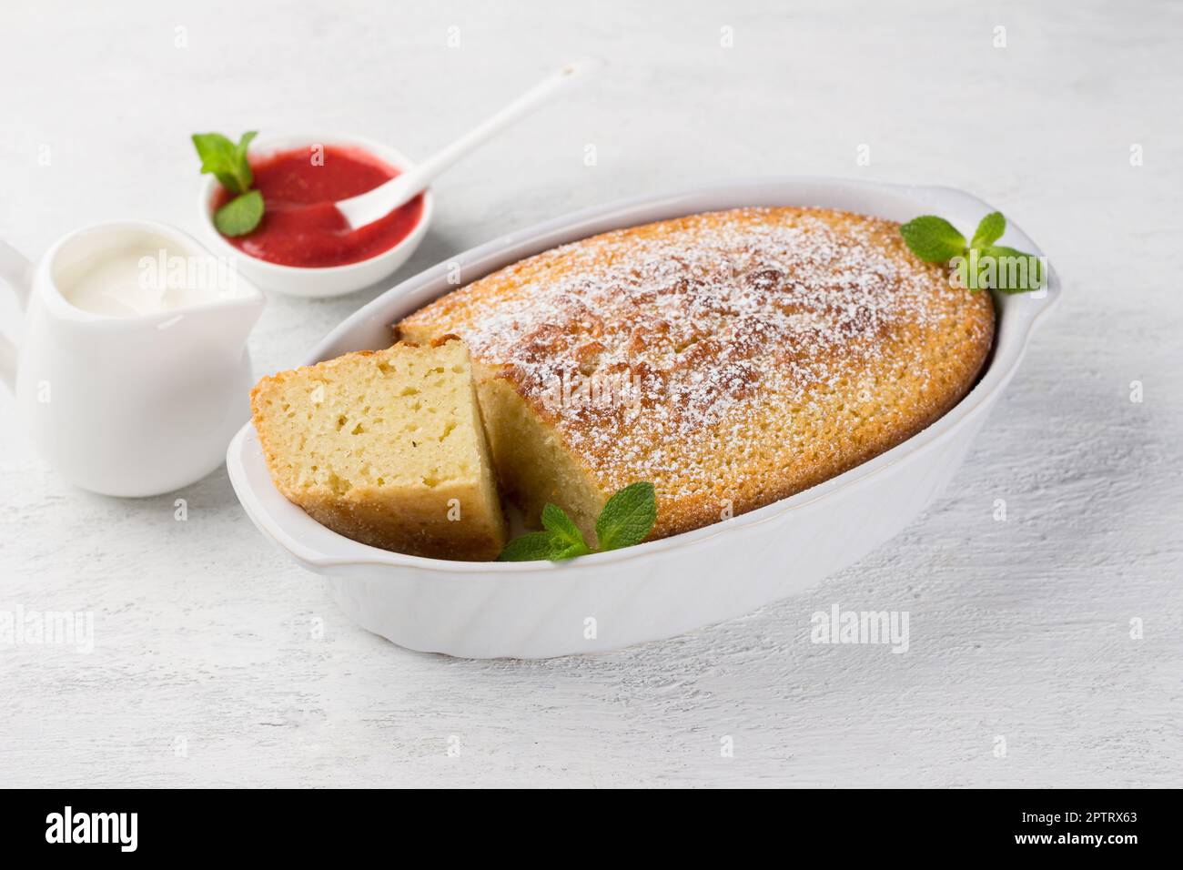 Mannik appena preparato, torta di semola in forma cosparsa di zucchero a velo con panna acida e salsa di frutti di bosco su fondo grigio chiaro Foto Stock