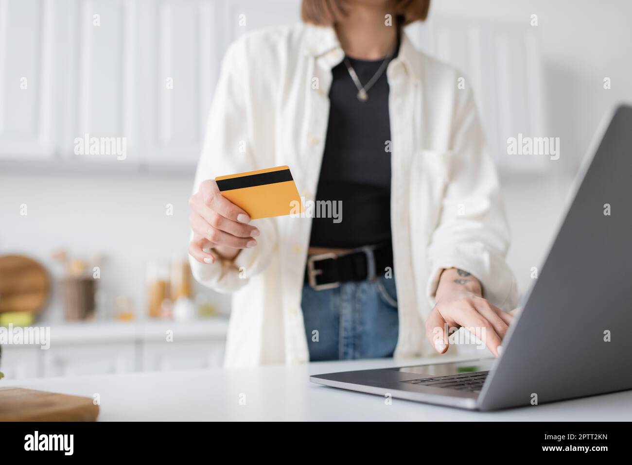 Vista ritagliata di una donna sfocata che tiene la carta di credito durante l'ordine di cibo sul notebook a casa, immagine stock Foto Stock