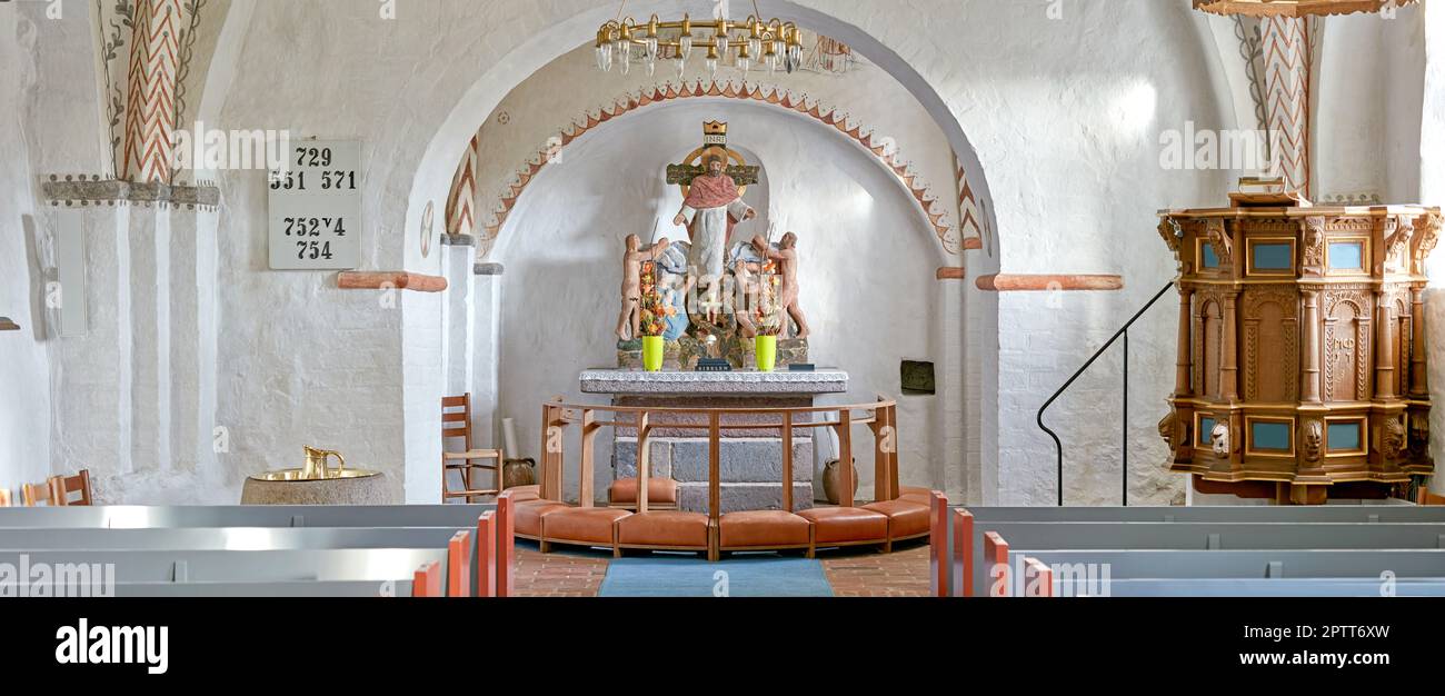 Interno di una chiesa storica con file di panchine, un pulpito, navata o alter con cuscini in ginocchio e la figura sacra di Gesù su una croce. 12th centur Foto Stock