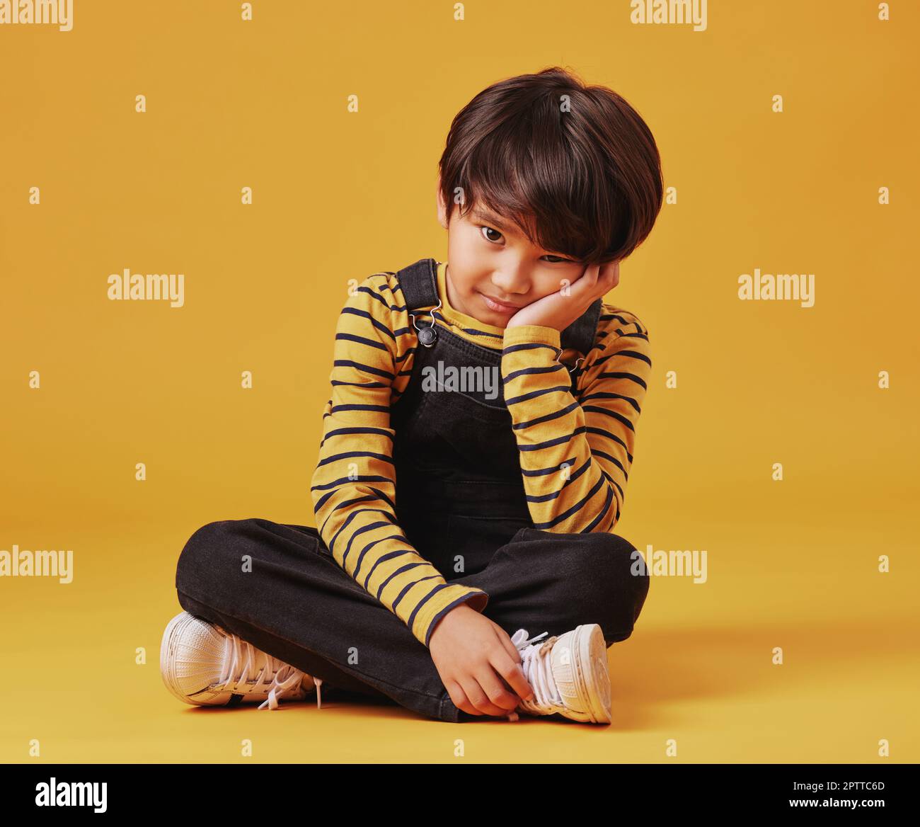 Un ragazzo asiatico che osserva triste e depresso mentre si siede sul pavimento e si posa contro sfondo arancione copyspace. Carino bambino misto gara con AGGIUNGERE look Foto Stock