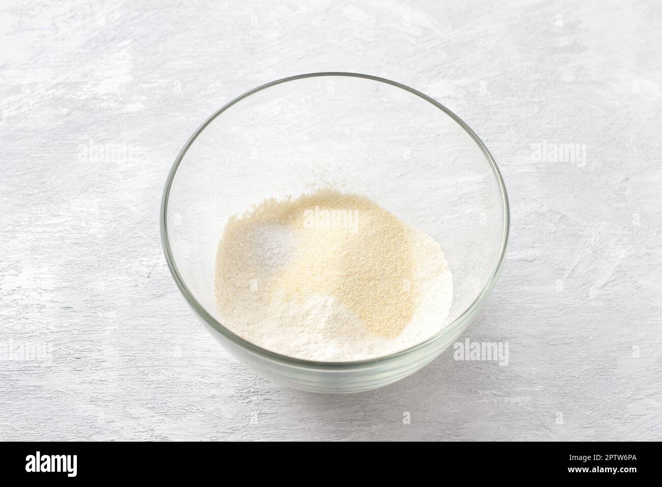 Ciotola di vetro con semola, farina, soda e sale su fondo grigio chiaro. Cucinare deliziose torte fatte in casa Foto Stock