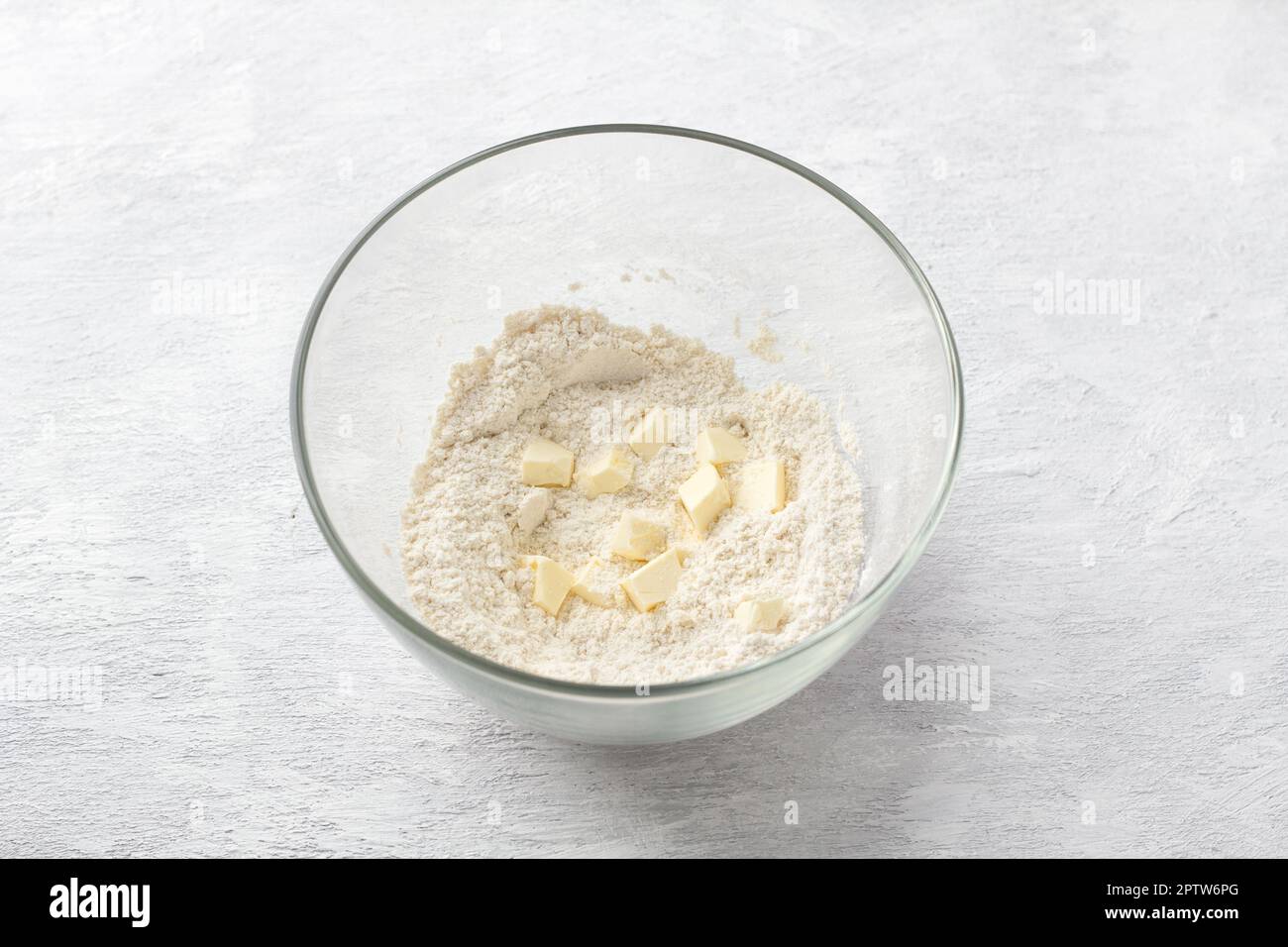 Ciotola di vetro con semola, farina e burro su fondo grigio chiaro. Cucinare deliziose torte fatte in casa Foto Stock
