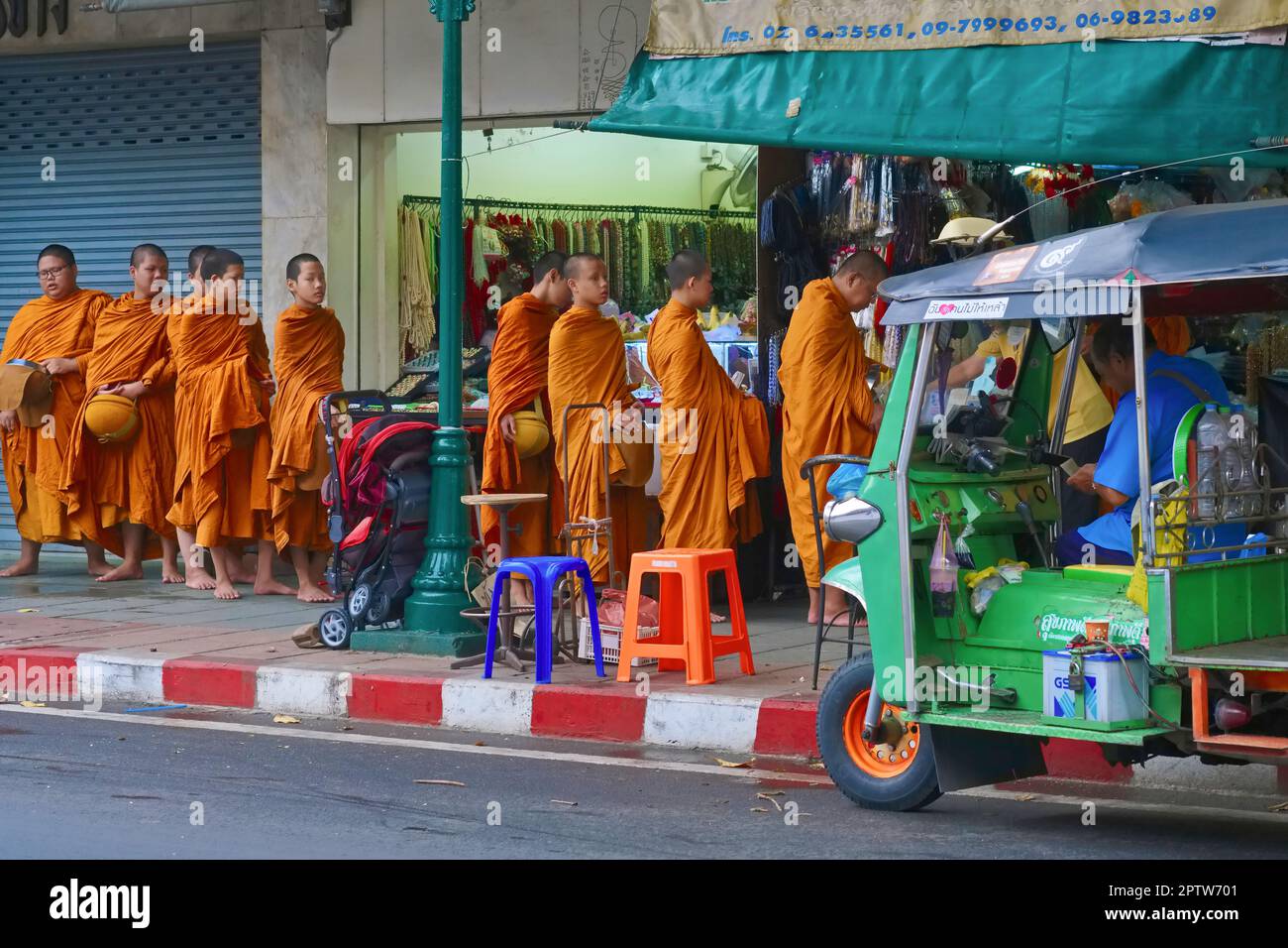 Monaci novizi buddisti che camminano per una strada in un file ordinato per ricevere le elemosine, passando un tuk-tuk sulla loro strada; Bangkok, Thailandia Foto Stock