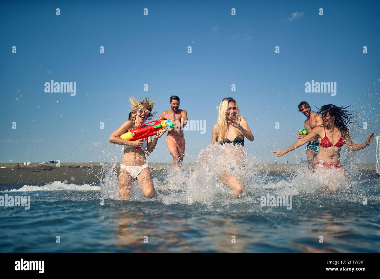 Gruppo di amici felici che hanno una pistola d'acqua lotta sulla spiaggia Foto Stock