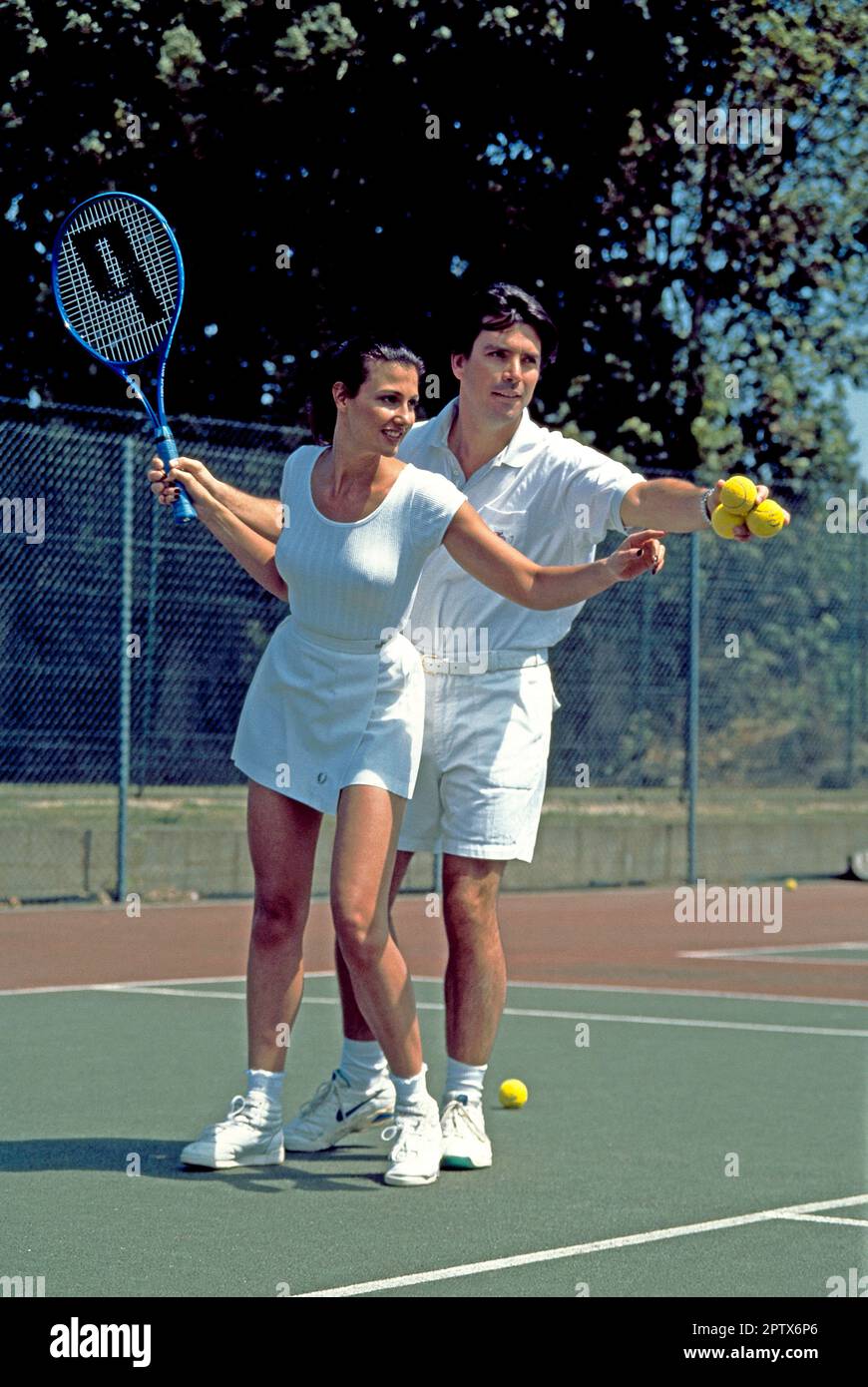 Uomo che insegna alla giovane donna come giocare a tennis. Foto Stock