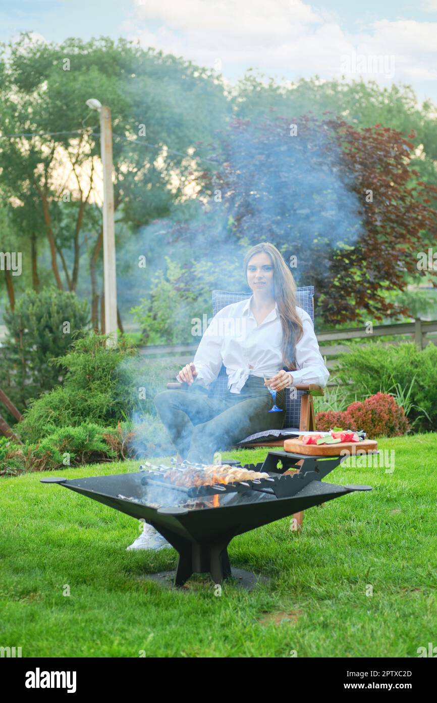 Donna carina che guarda le verdure alla griglia sul barbecue Foto Stock