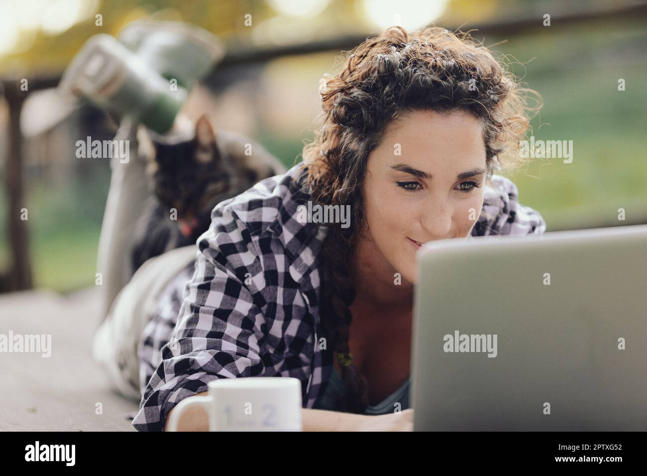 Mentre si gode liberamente la natura sdraiata su un tavolo per divertirsi e giocare con il suo pc, una ragazza si ritrova con un gatto sulla schiena. Naughty profittatore, come dar Foto Stock