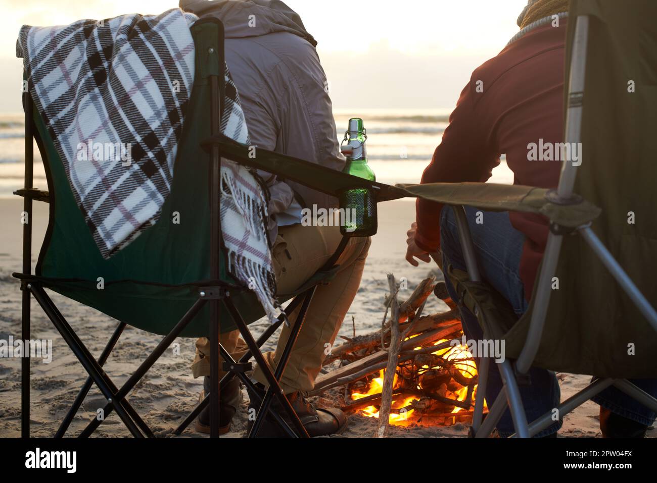 Niente di meglio di una birra una birra una birra. Due giovani seduti attorno ad un fuoco sulla spiaggia Foto Stock