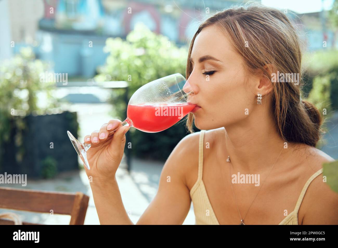 Carina giovane donna beve limonata di cocomero freddo alla terrazza esterna in caldo giorno di sole Foto Stock