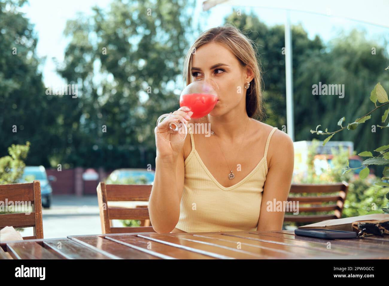 Bella giovane donna beve limonata di fragole fredda sulla terrazza all'aperto in calda giornata di sole Foto Stock