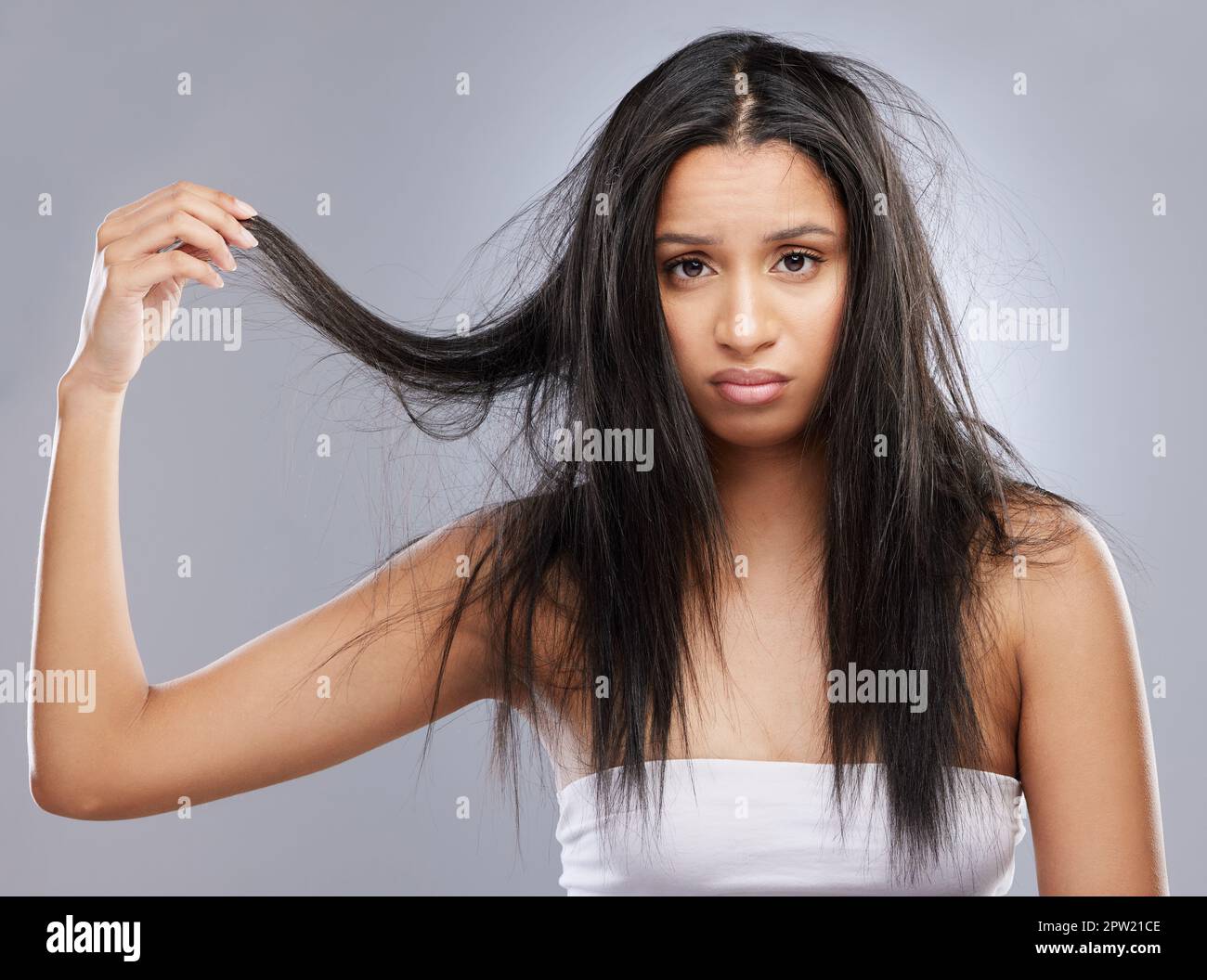 Avete qualche consiglio per i capelli danneggiati? Studio di una giovane donna con capelli danneggiati che si posano su uno sfondo grigio Foto Stock