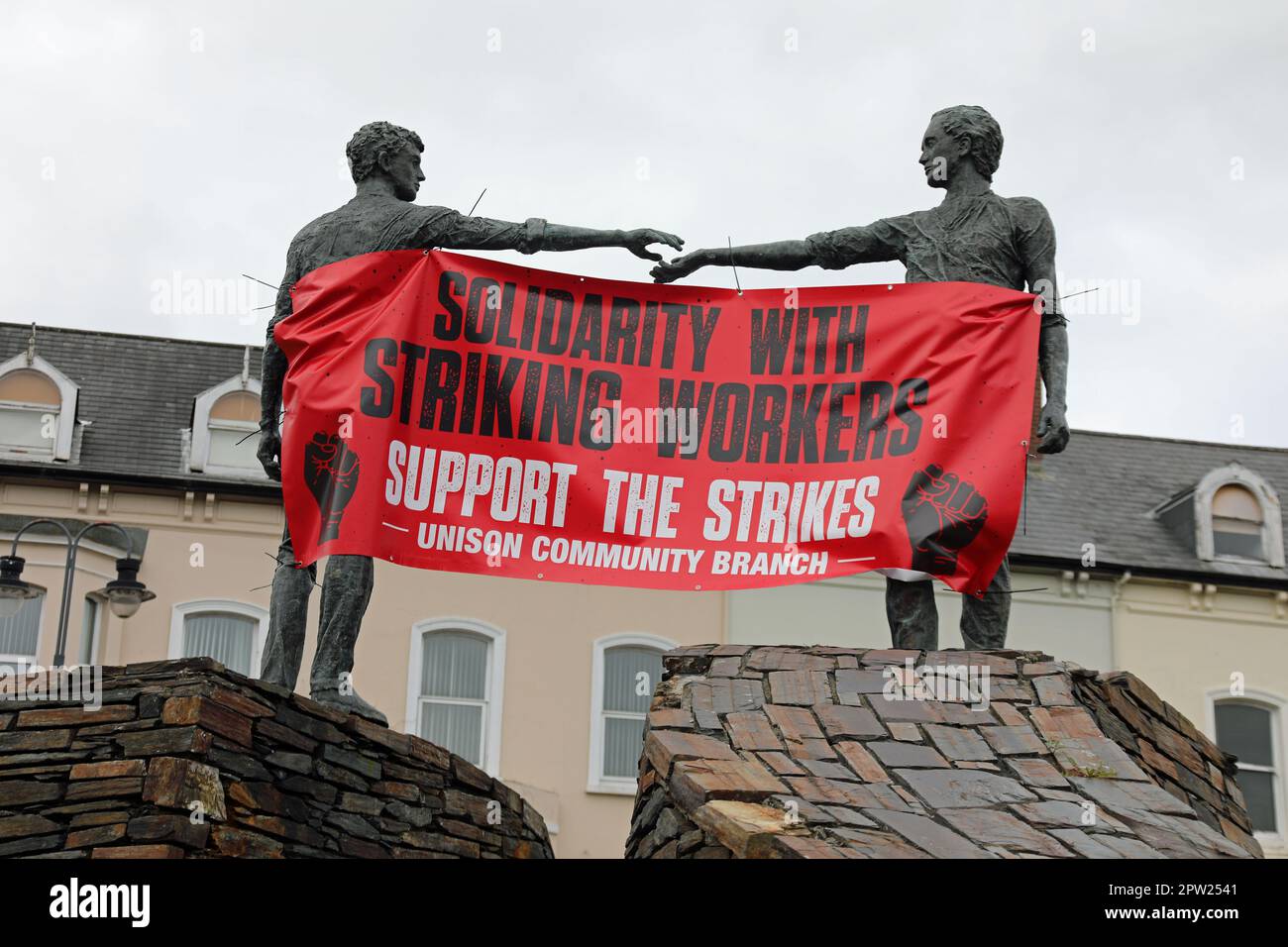 Banner sindacale drappeggiato tra le mani attraverso la scultura divide in Derry Foto Stock