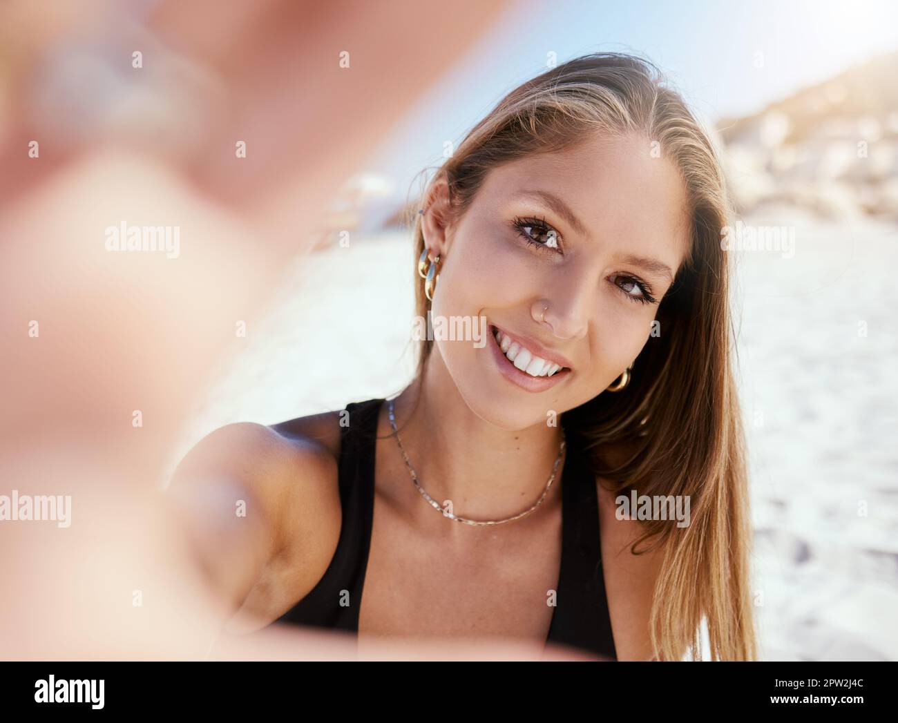 Una bella giovane donna caucasica che si rilassa e scatta una foto al selfie mentre si siede sulla spiaggia. Godetevi una vacanza estiva o una vacanza all'aperto Foto Stock