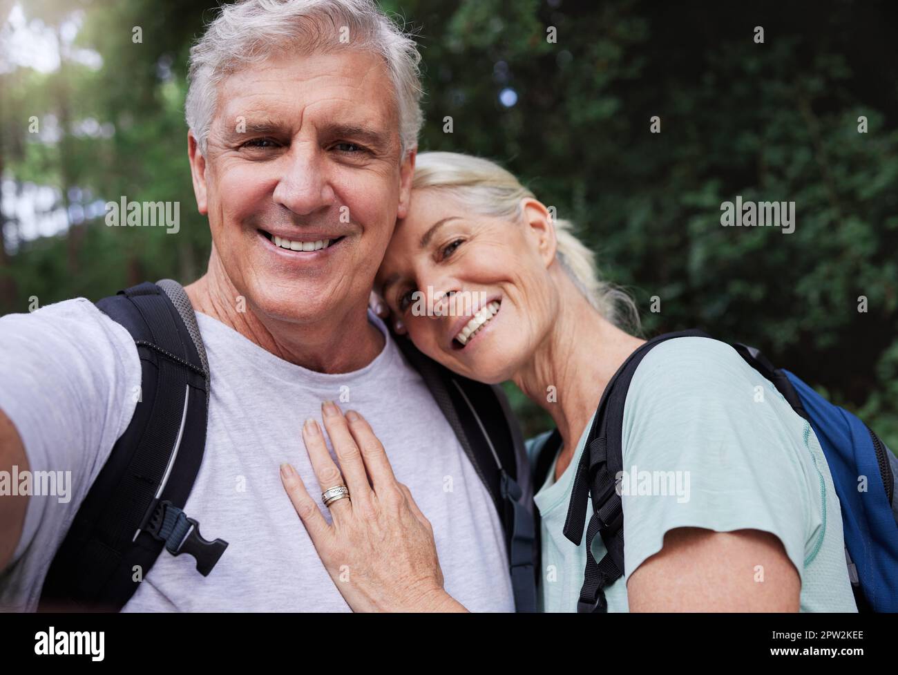 Ritratto di una coppia caucasica anziana sorridente e scattante un selfie in una foresta durante un'escursione all'aperto. Uomo e moglie che mostrano affetto e holdin Foto Stock