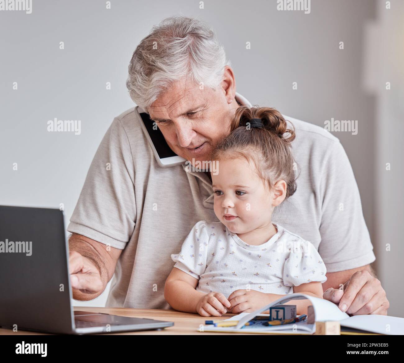 Uomo anziano, bambino e telefonata mentre lavora su un computer portatile per lavorare in remoto con la ragazza di baby sitter nonno in ufficio a casa. Maschio con bambino come famiglia dentro Foto Stock