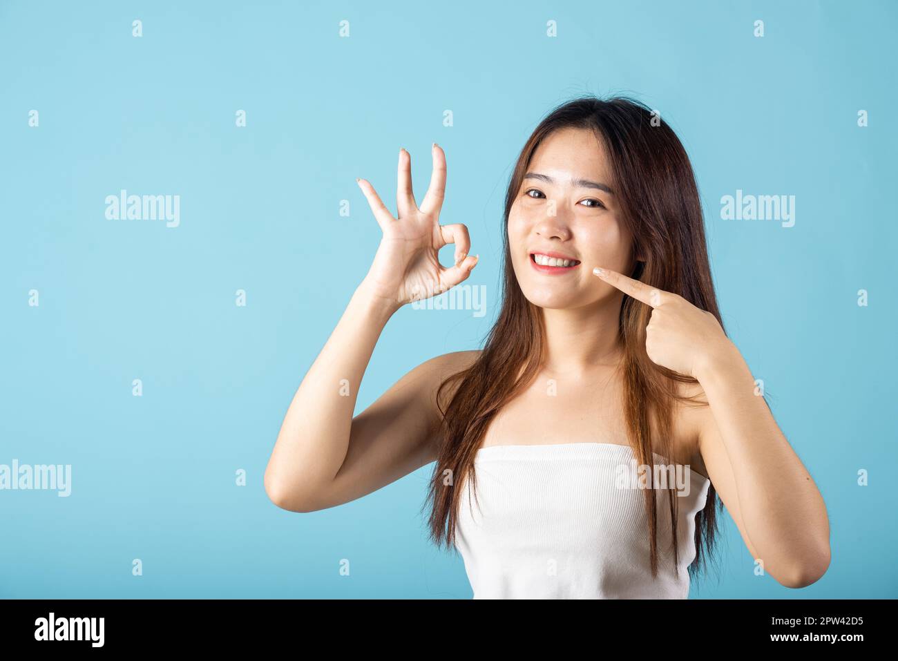 Concetto di salute dentale. Giovane donna asiatica che indica i suoi forti denti bianchi e mostrando OK segno per una buona ripresa in studio isolato su sfondo blu, Beau Foto Stock