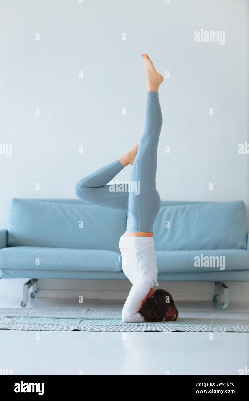 Femmina sottile in abbigliamento sportivo che si piega da parte mentre si pratica yoga vicino divano a casa Foto Stock