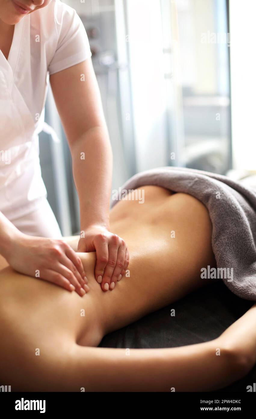 Master senza volto che dà massaggio di muscoli della schiena e delle spalle a. donna anonima sdraiata sul tavolo nel salone termale Foto Stock