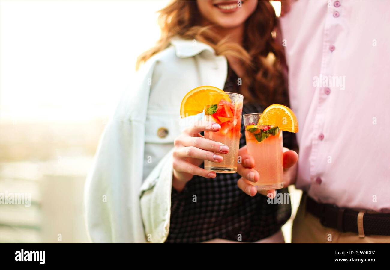 Uomo e donna anonimi, sorseggiando bicchieri di cocktail di frutta e proponendo toast durante la data romantica Foto Stock