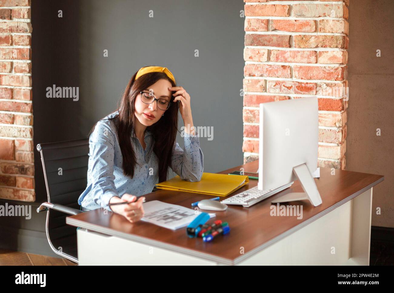 Giovane donna manager in occhiali digitando sulla tastiera netbook mentre si siede al tavolo e lavora in un ufficio moderno Foto Stock