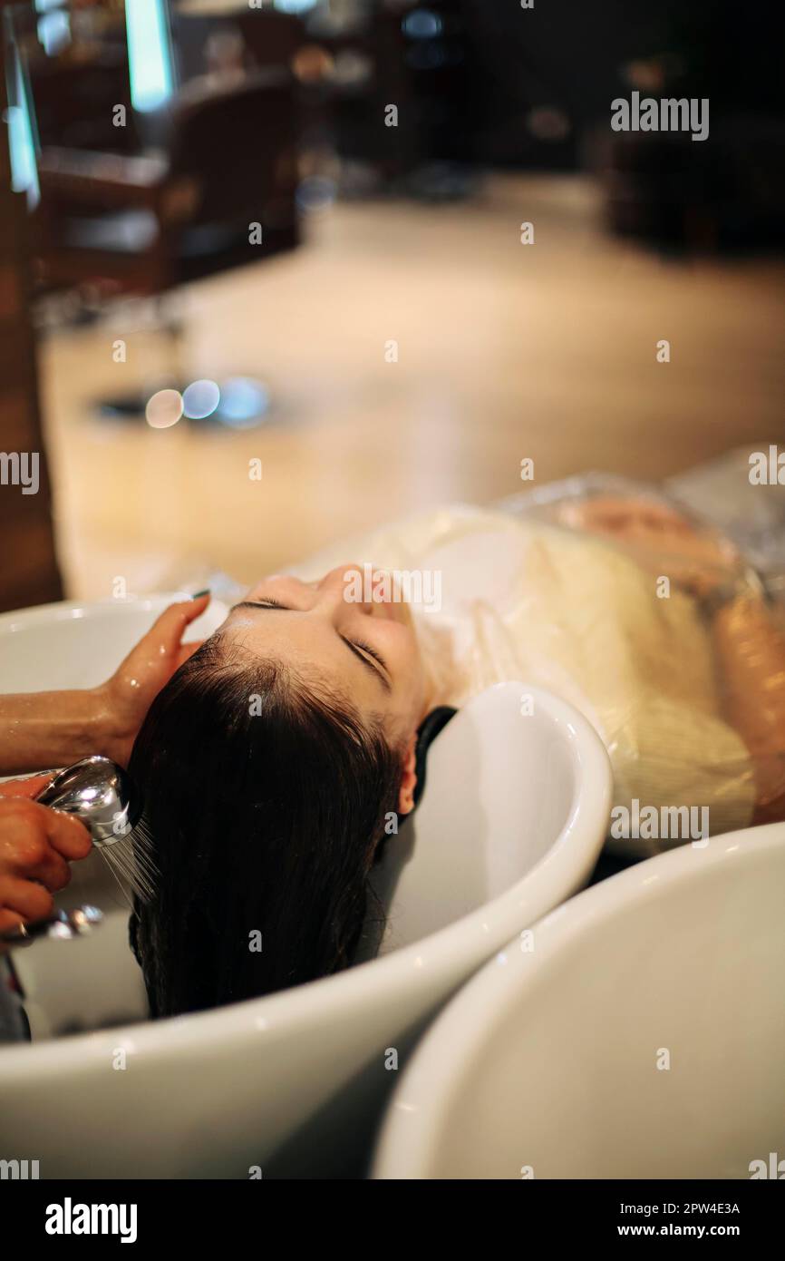 Giovane donna allegra che ama il massaggio alla testa mentre si lava i capelli da un parrucchiere professionista. Bellezza, acconciatura, moda, stile di vita Foto Stock