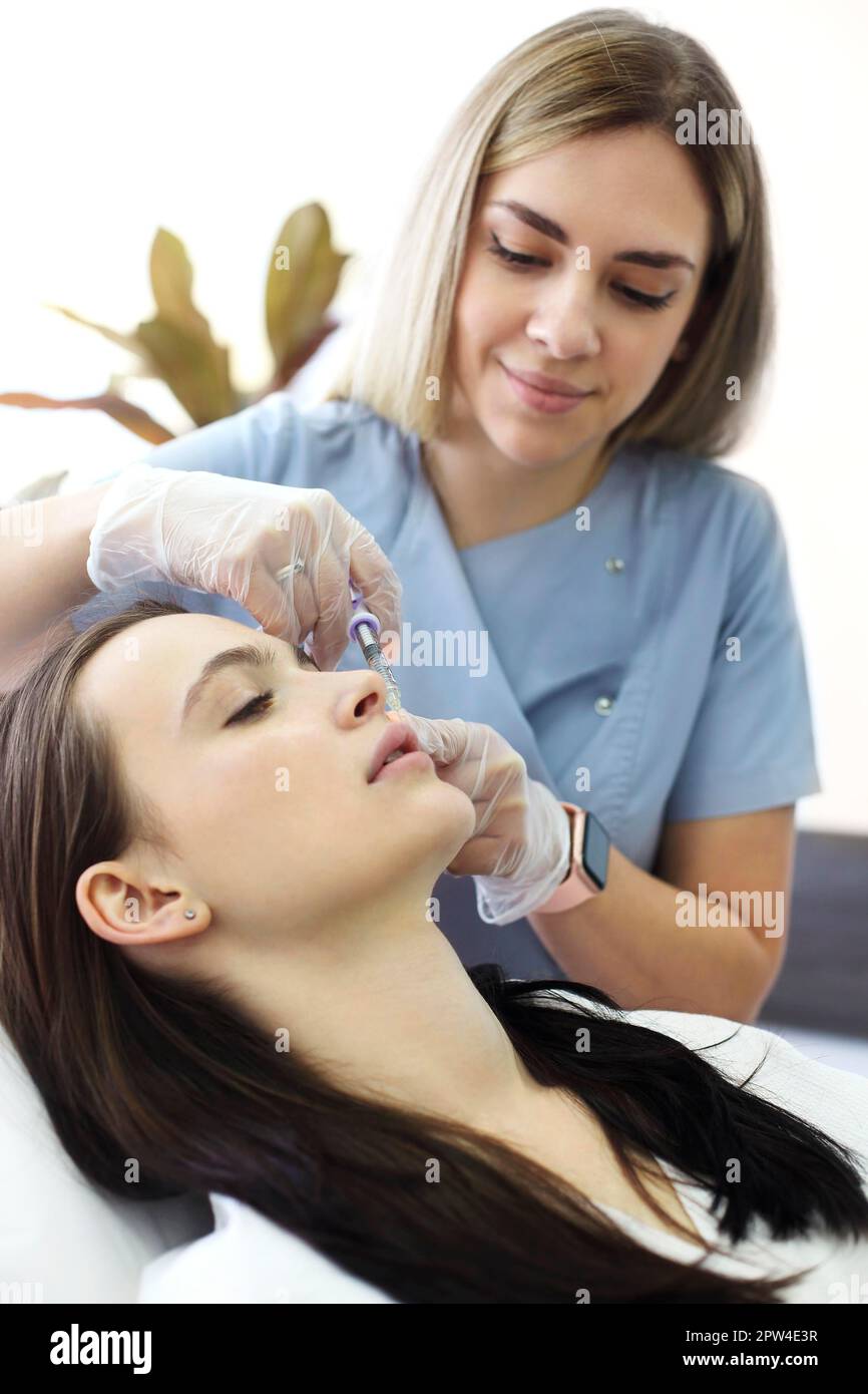 Estetista professionista che inietta acido ialuronico vicino agli occhi della donna durante procedura anti invecchiamento in clinica di bellezza Foto Stock