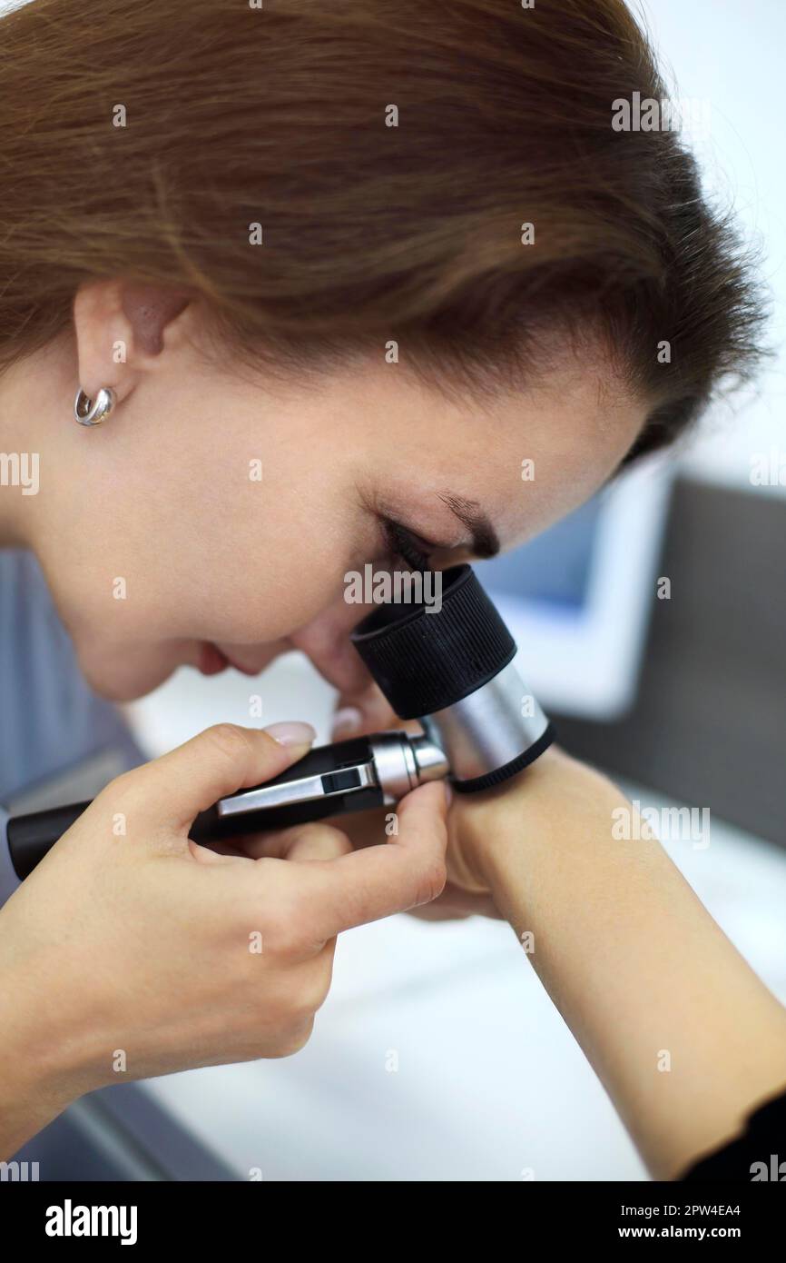 Foto ravvicinata della giovane dermatologa bruna donna esamina nevo o segni di nascita su pazienti mano con dermatoscopio. Prevenzione del melanoma, mole Foto Stock