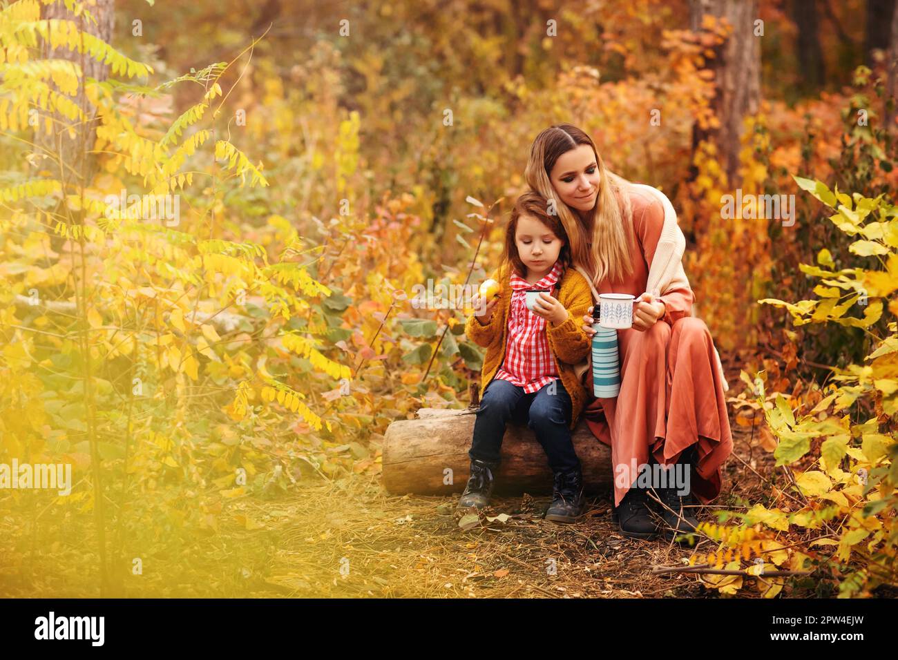 Giovane famiglia, madre e bambina, in abiti eleganti gustando una bevanda calda mentre si siede nella foresta autunnale Foto Stock