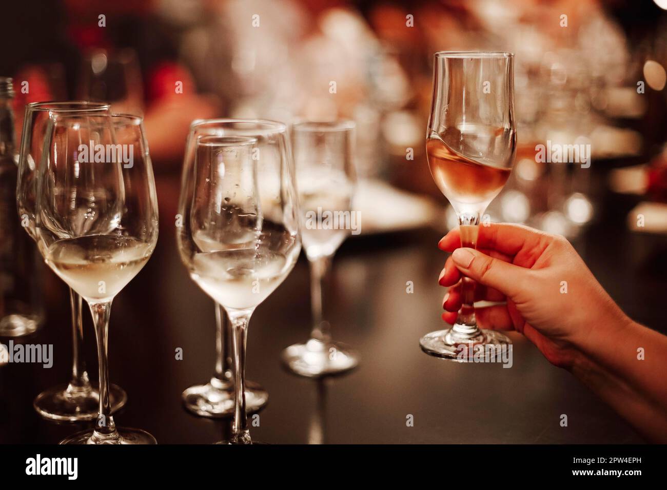 Bicchieri con diversi tipi di vino e mani umane che tengono i bicchieri da vino sullo sfondo. Degustazione di vini Foto Stock