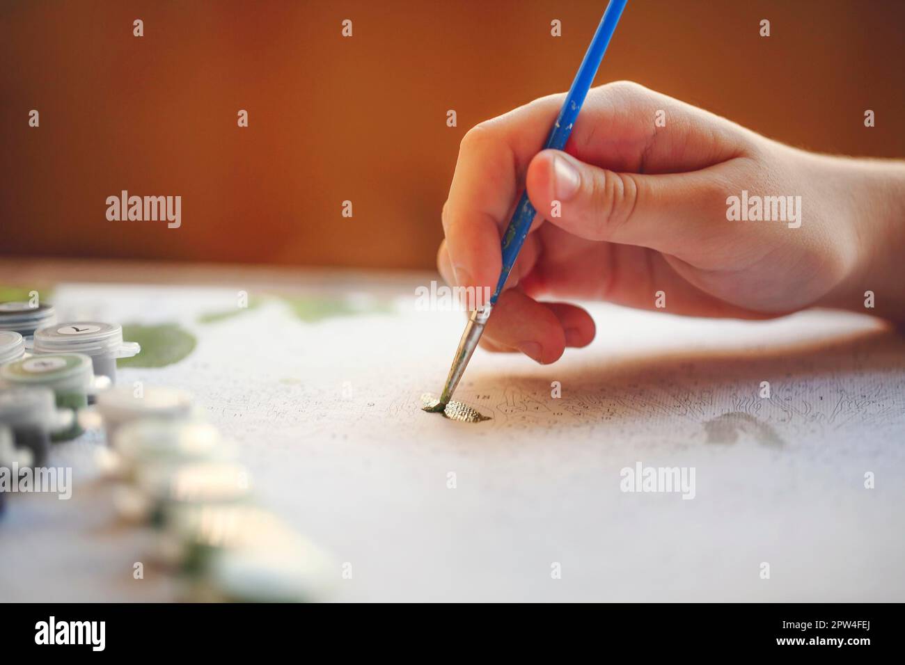 Foto ritagliata sfocata di pittura a mano femminile con pennello su carta, fuoco selettivo sulle vernici acriliche in scatole di plastica disposte in fila secondo Foto Stock