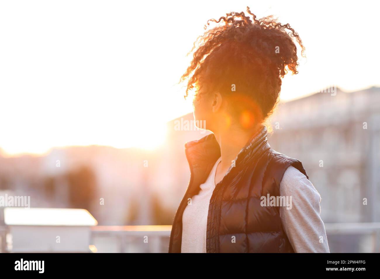 Vista posteriore della giovane donna in piedi sul tetto alla luce del sole del mattino, afro-americana donna in piedi sul tetto e godere di una nuova bella giornata mentre Foto Stock