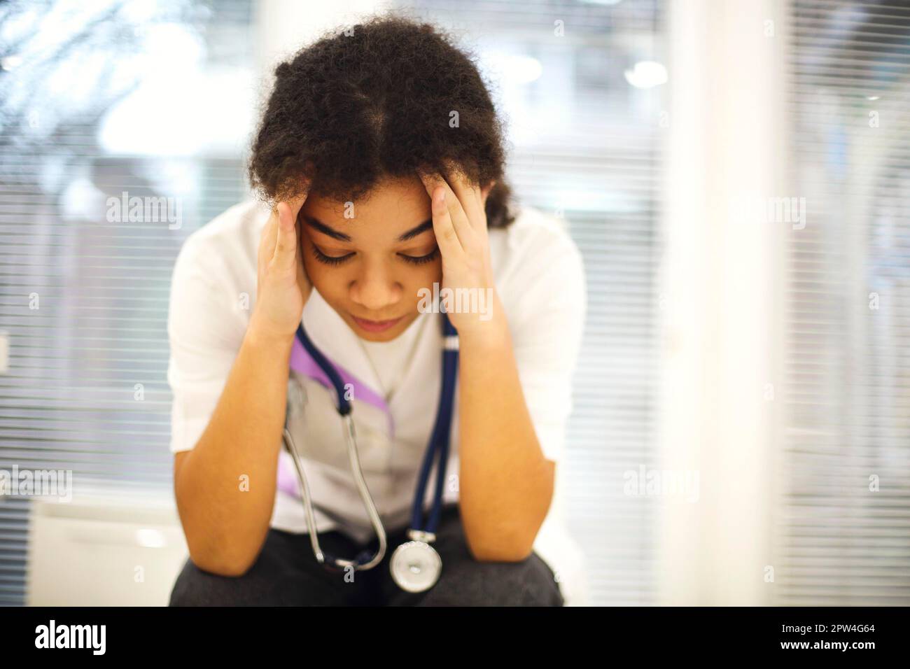 Triste depresso giovane afroamericana infermiera seduta con frustrata espressione del volto, sensazione di essere sopraffatta dal carico di lavoro in clinica, medico di etnia femminile Foto Stock