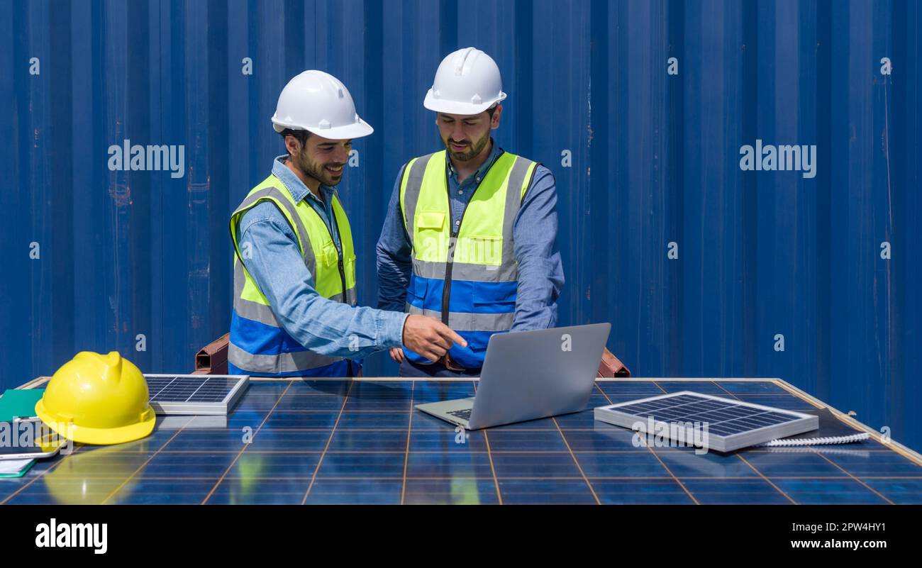 Addetto alla spedizione che indica il programma di spedizione sul computer portatile, spiega al collega la pianificazione della spedizione successiva. Utilizzano pannelli a celle solari A. Foto Stock