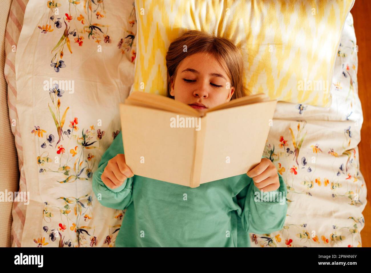 Ragazza adolescente caucasica bionda è sdraiata sul letto e libro di lettura. Lettura di fiction, hobby, attività di svago e ricreazione. Concetto di casa Foto Stock