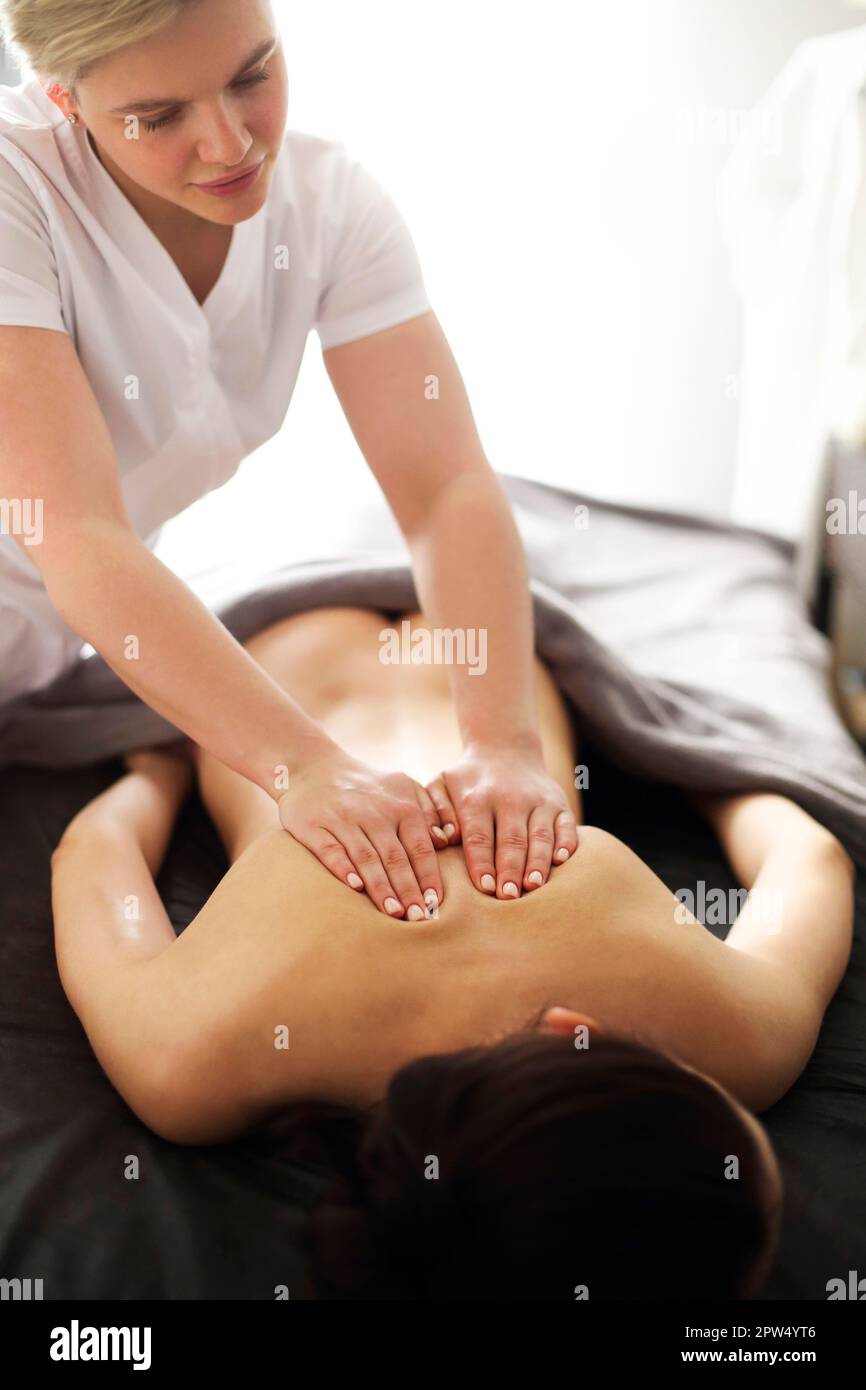 Master senza volto che dà massaggio di muscoli della schiena e delle spalle a. donna anonima sdraiata sul tavolo nel salone termale Foto Stock