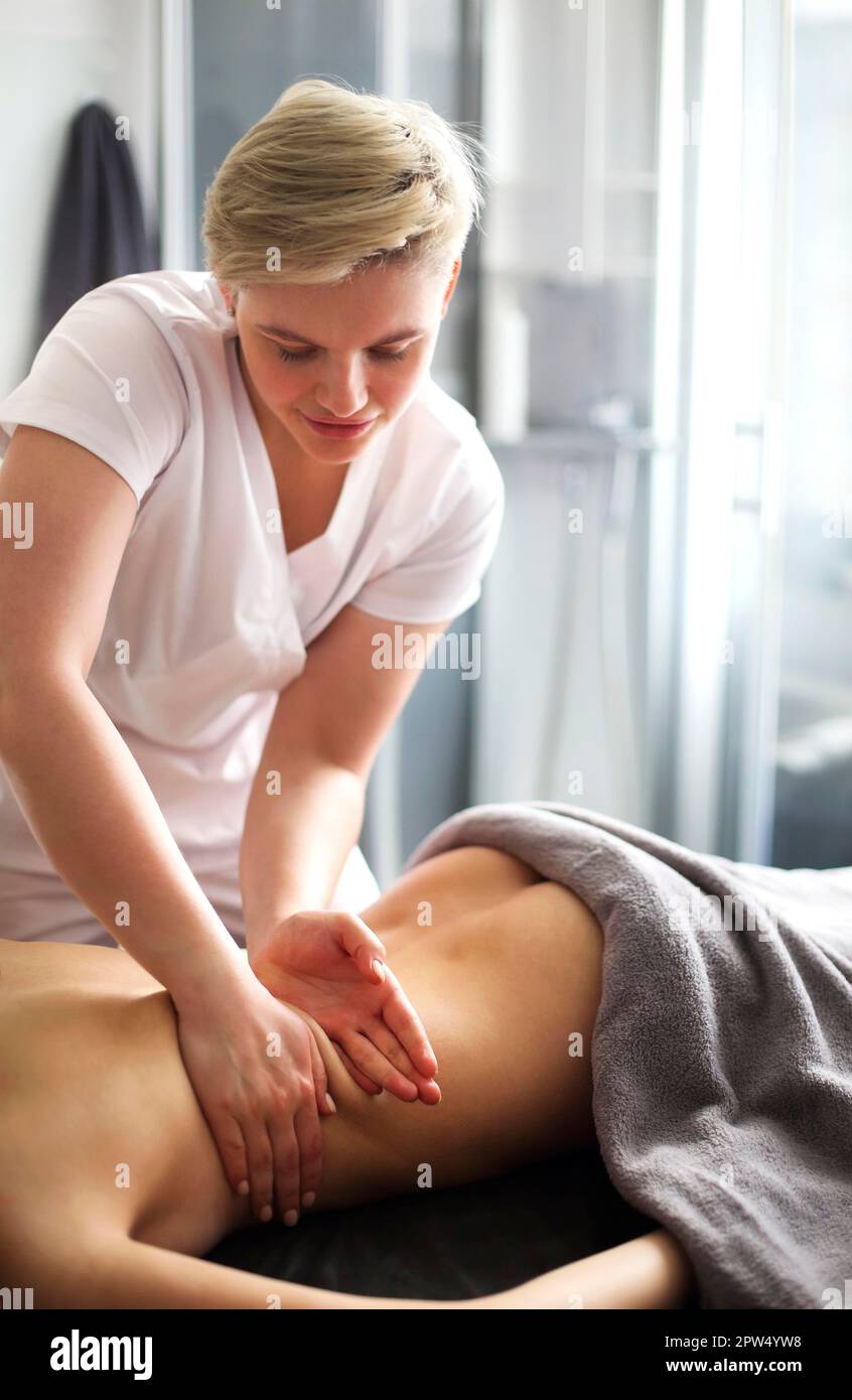 Master senza volto che dà massaggio di muscoli della schiena e delle spalle a. donna anonima sdraiata sul tavolo nel salone termale Foto Stock