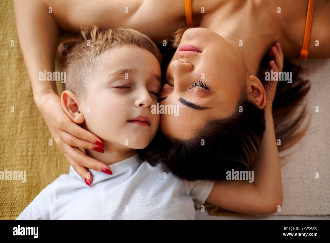 Vista dall'alto di giovane madre e figlio di famiglia positiva che ride e abbraccia mentre sdraiato a letto e godendo i momenti felici insieme, carino ragazzino Foto Stock