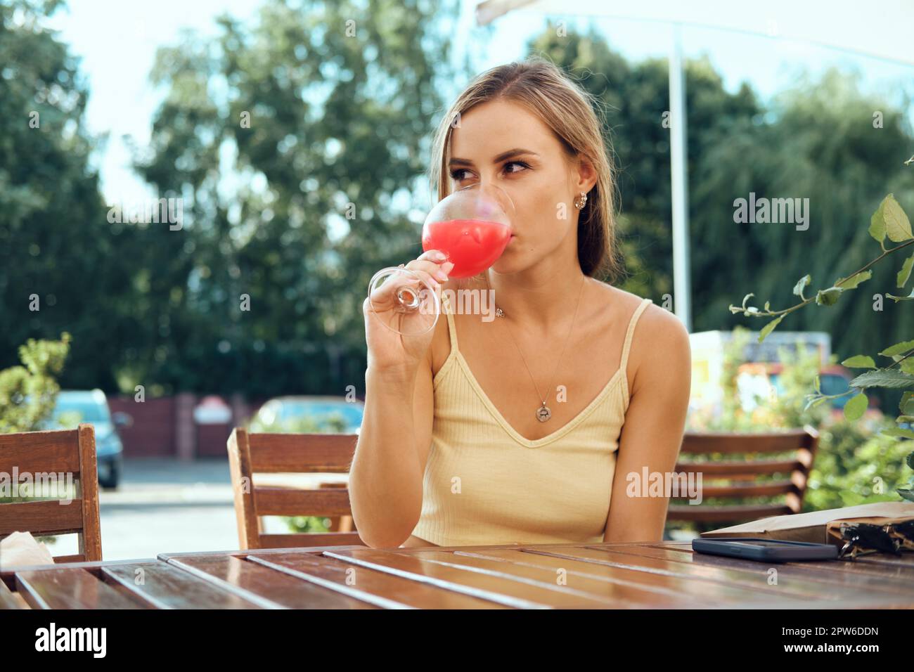 Bella giovane donna beve limonata di fragole fredda sulla terrazza all'aperto in calda giornata di sole Foto Stock