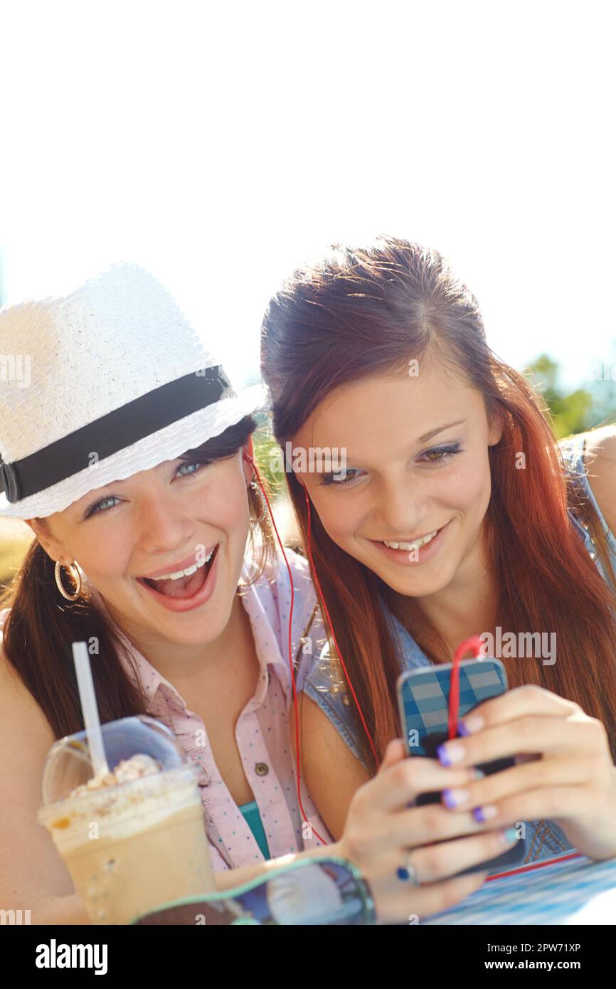 Alla scoperta di nuove band insieme. Due ragazze adolescenti che condividono gli auricolari mentre ascoltano la musica su un telefono cellulare Foto Stock