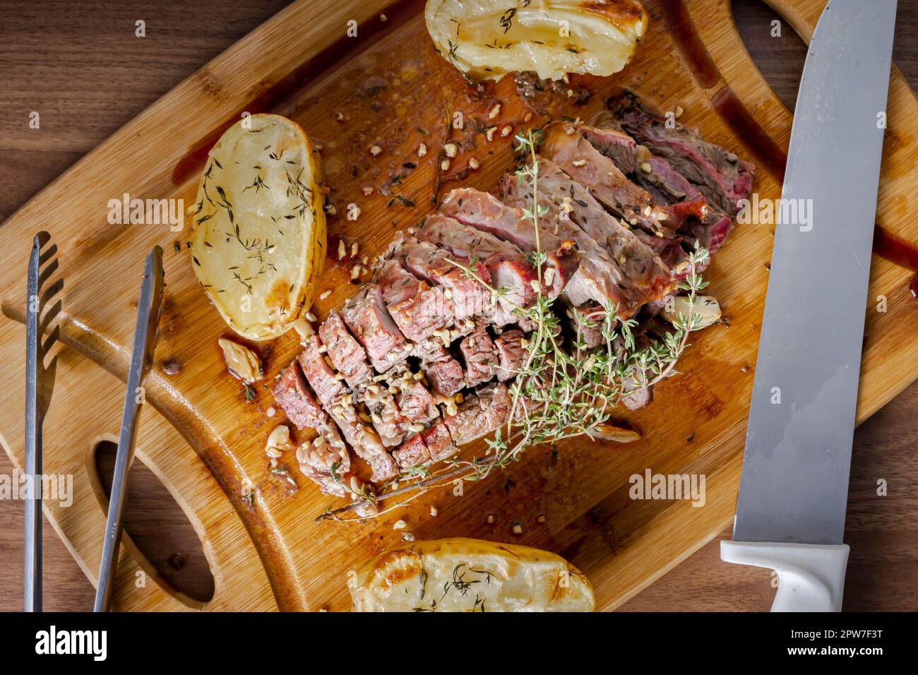 FLANK STEAK Beef BBQ food. Carne arrosto con patate e timo su un asse di legno, completamente tagliata a fette. Vista dall'alto. Foto Stock