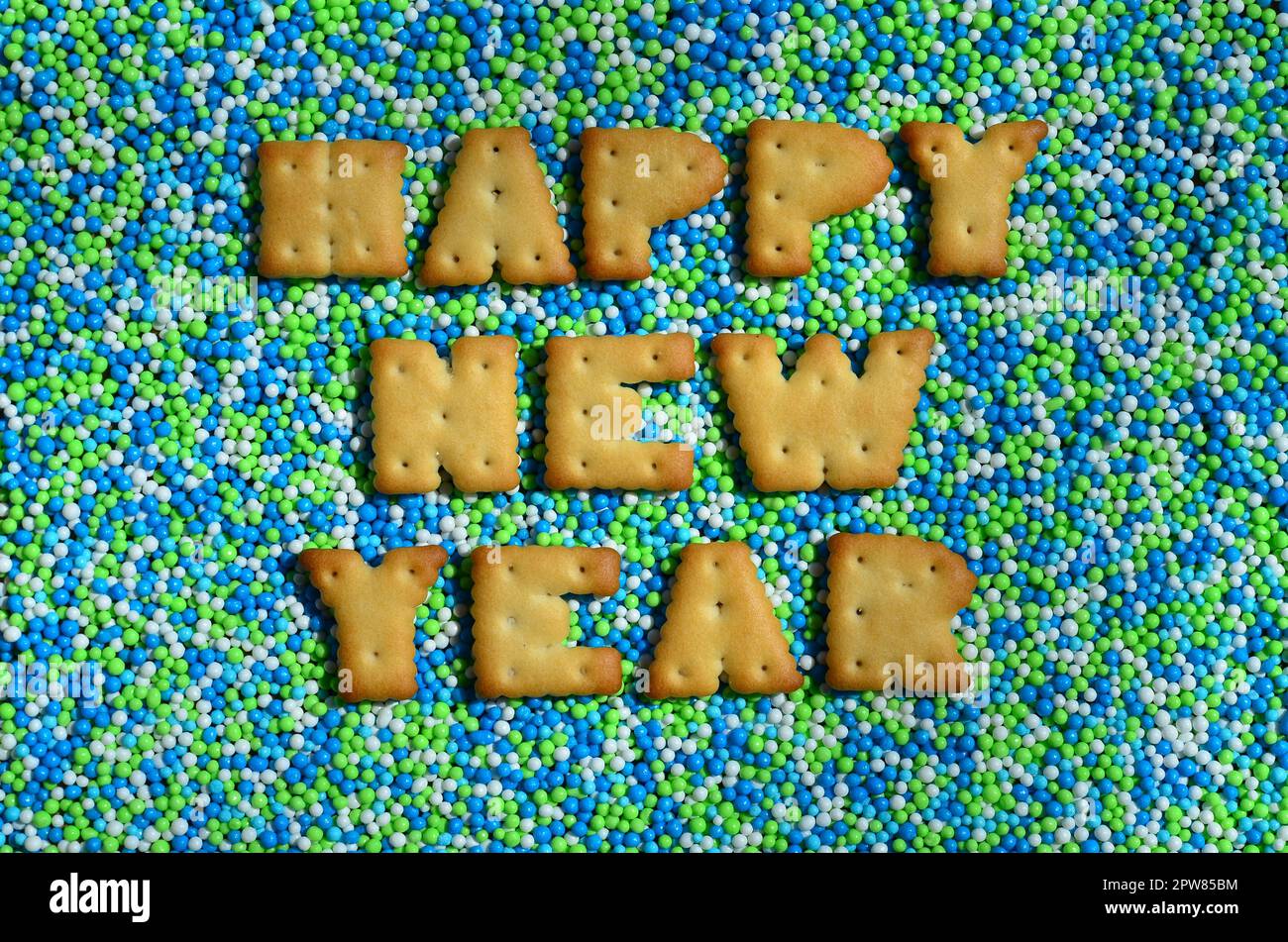 Felice anno nuovo. La parola dalle lettere commestibili del cracker si trova sulla polvere smaltata. Un enorme numero di dolci, colorate perle di dimensioni molto piccole per il deco Foto Stock